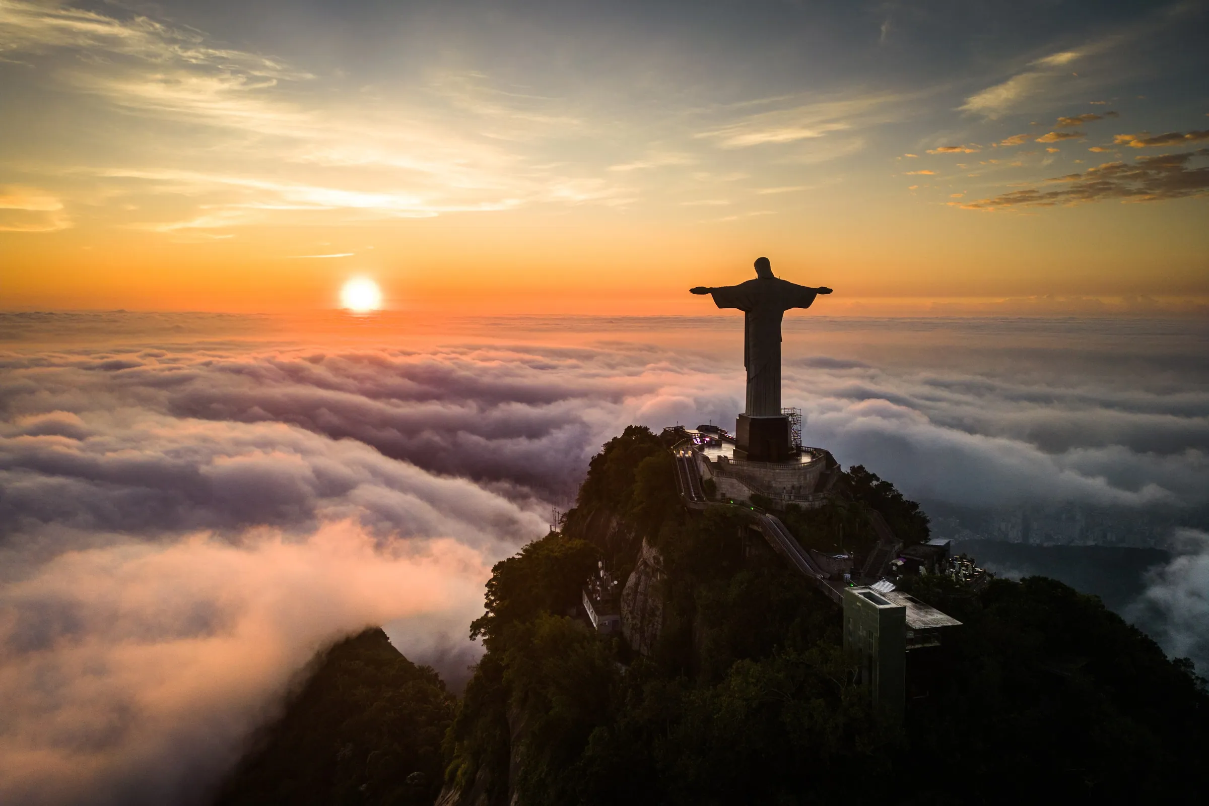The Christ the Redeemer statue on its rocky peak at sunrise, rising above a sea of clouds in Rio de Janeiro