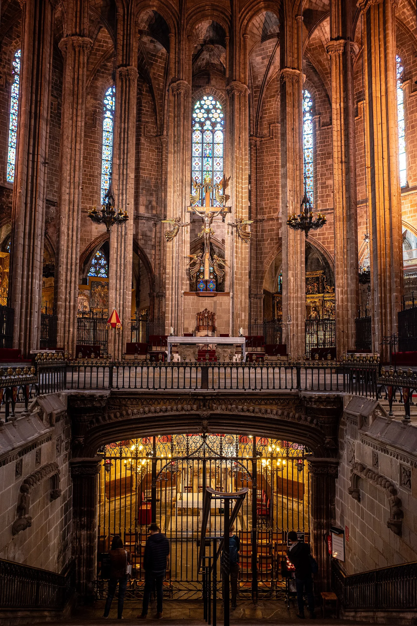 The Gothic nave of Barcelona Cathedral with pointed arches, hanging lamps, and a carved choir balustrade in the foreground
