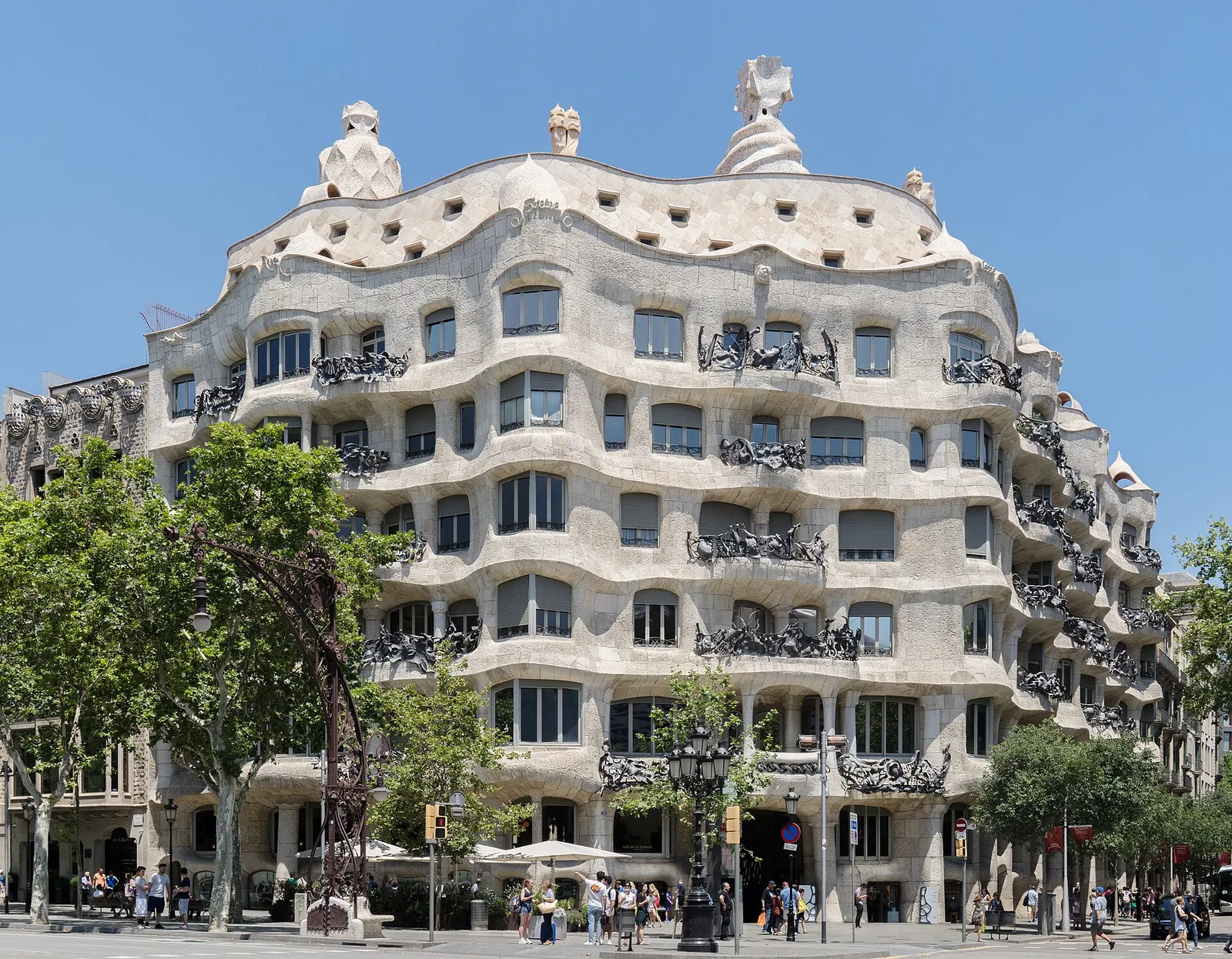 The undulating stone facade of La Pedrera (Casa Milà) with wrought-iron balconies, seen from the street under a blue sky