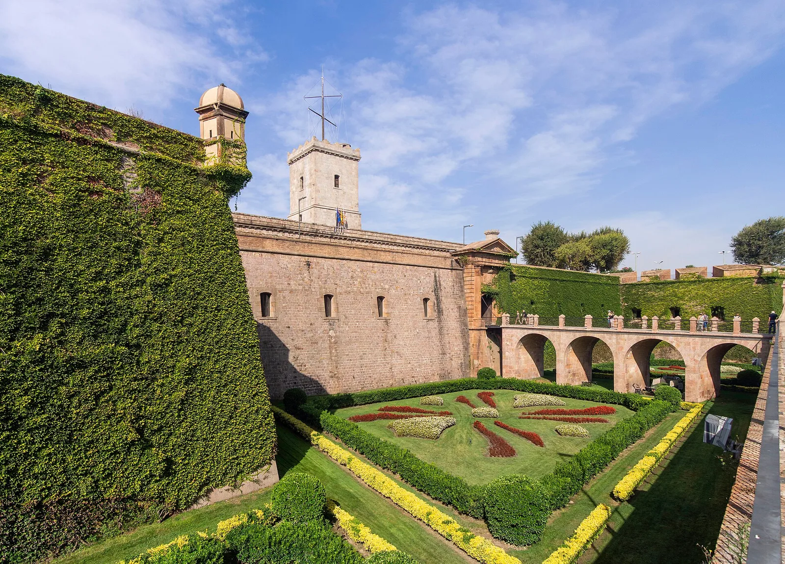 The ivy-covered walls and formal garden of Montjuïc Castle under a blue sky