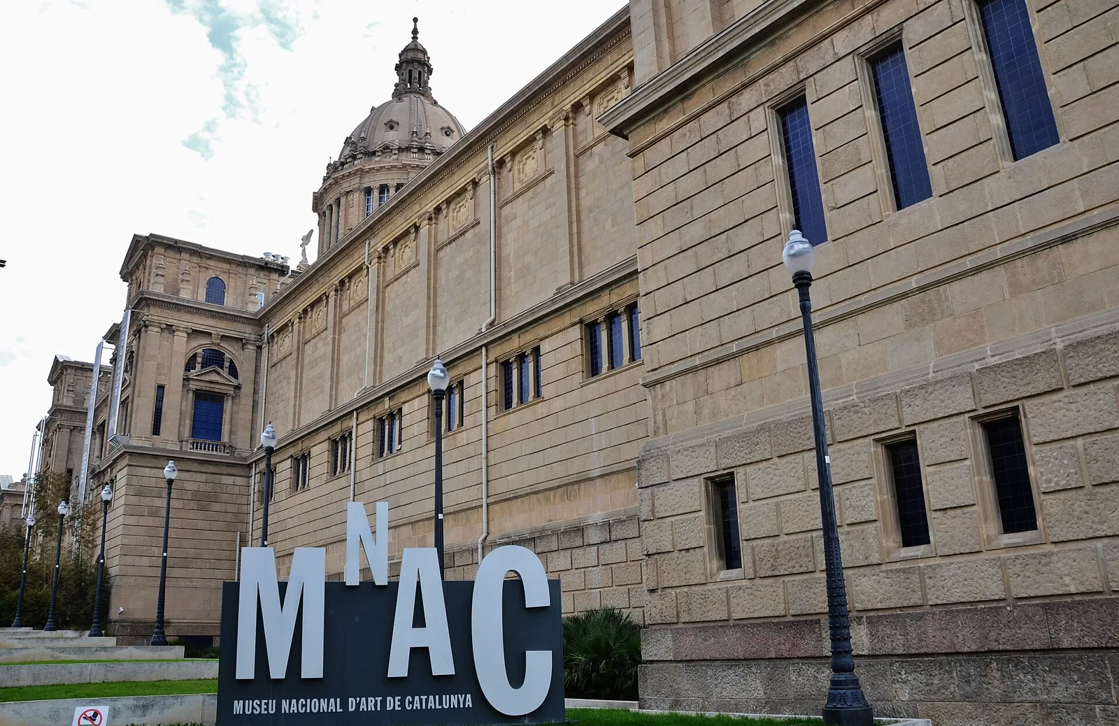 The sandstone facade of the Museu Nacional d’Art de Catalunya with the MNAC sign in the foreground