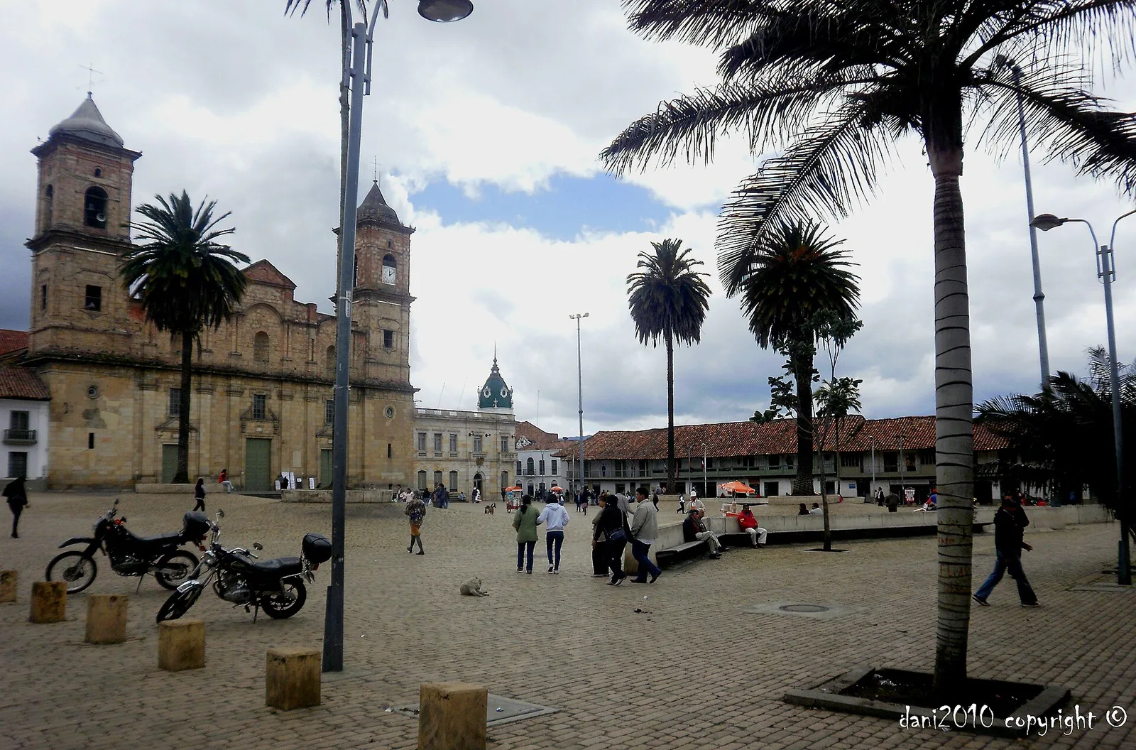 A plaza in Zipaquirá with a twin-towered church, palm trees, and parked motorcycles