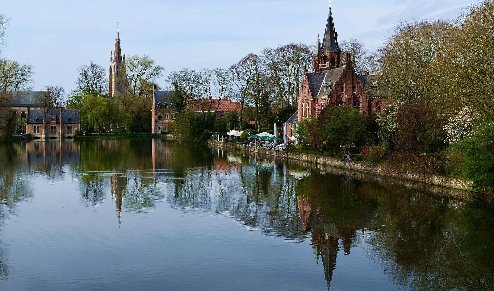 Red-brick houses and a church spire reflected in the still water of Minnewater