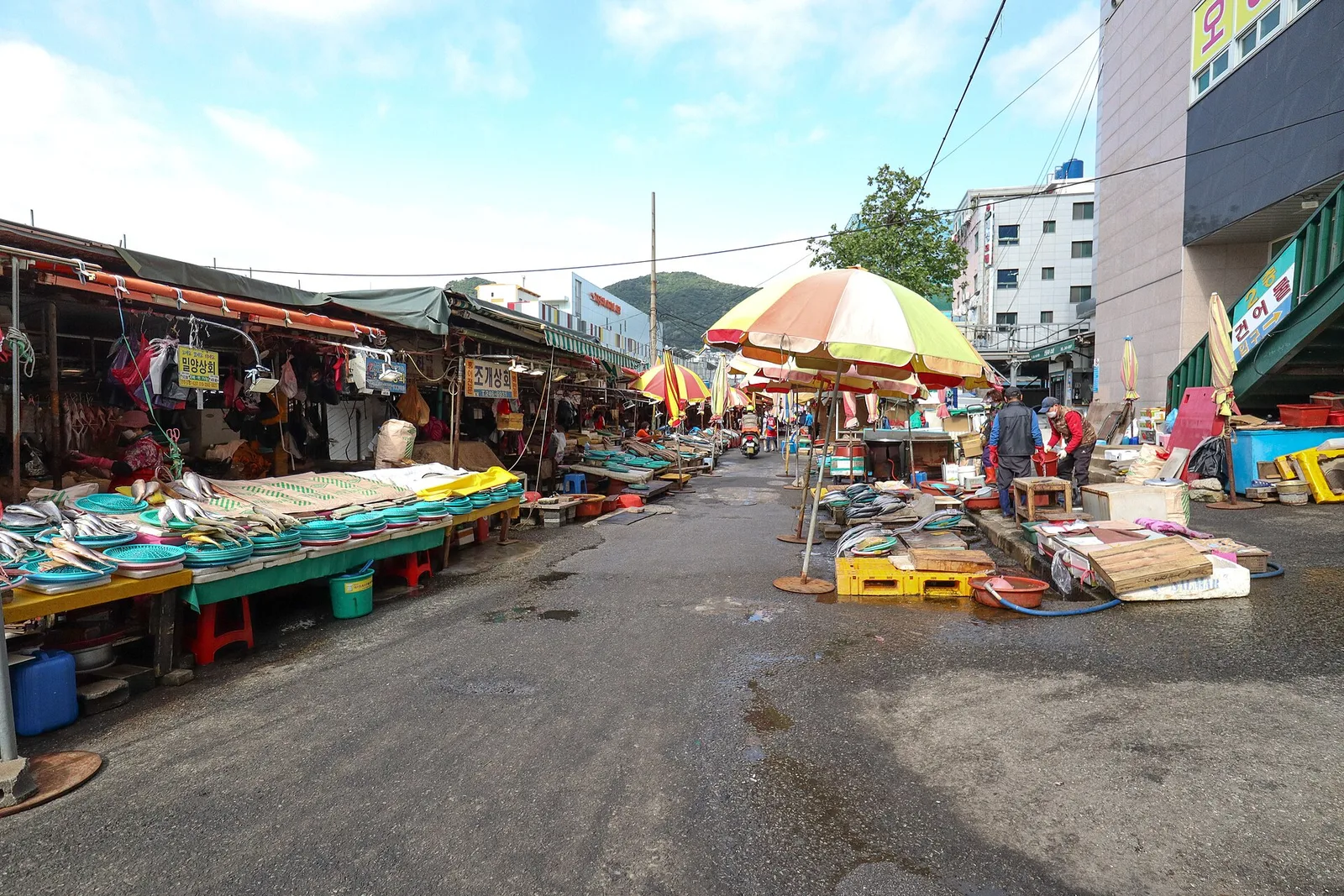 A street of covered market stalls in the Jagalchi Market area, with buildings and hills behind