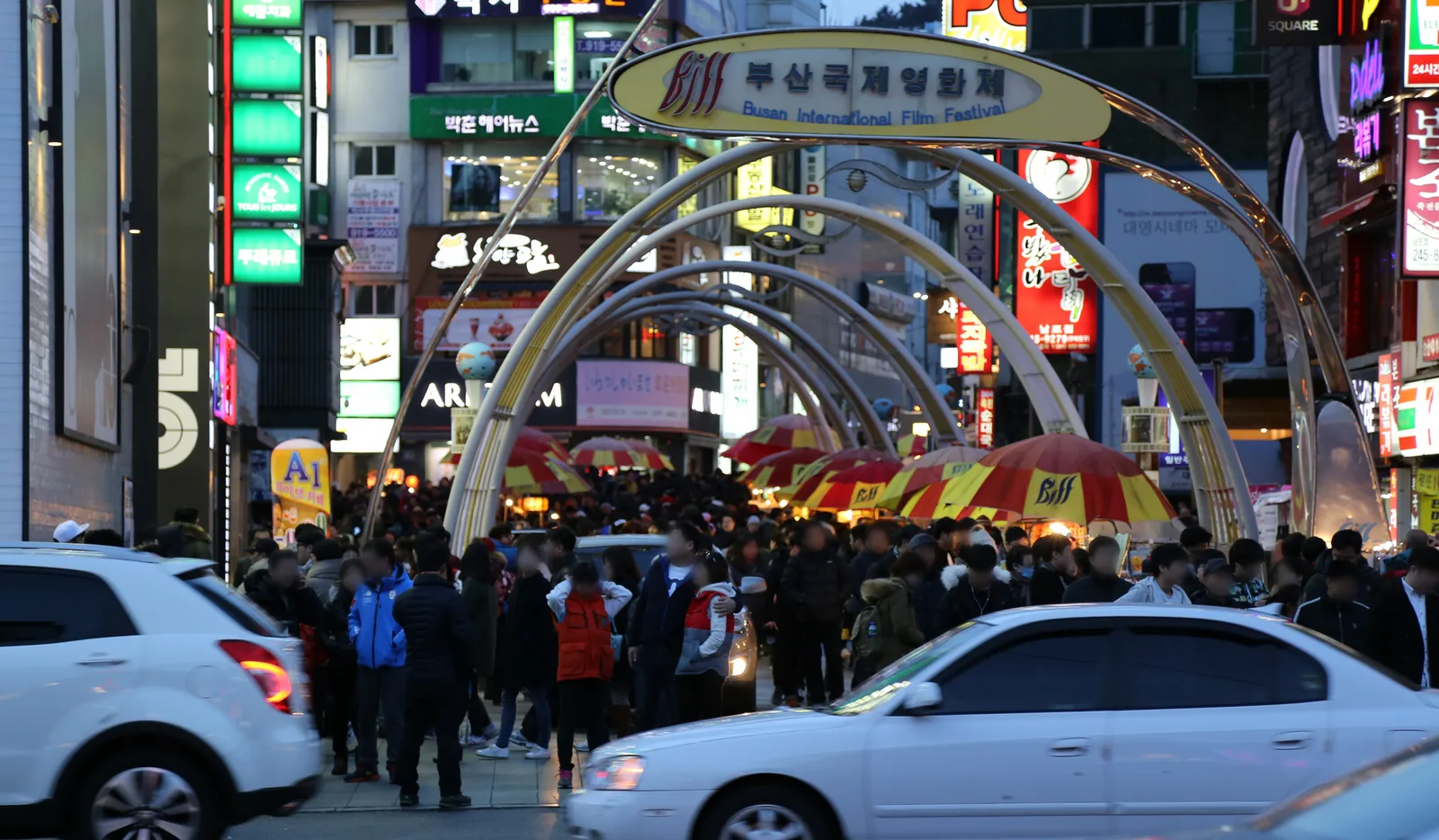 A neon-lit gateway arch and crowded street in BIFF Square