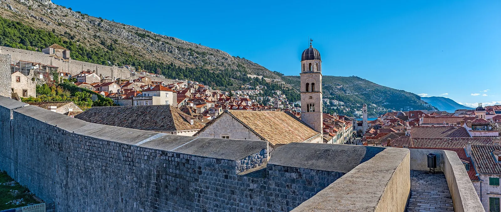 The Old Town's stone walls and a walkway, with the Franciscan bell tower and red roofs behind