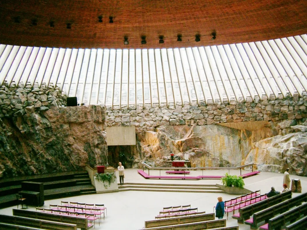 The interior of Temppeliaukio Church, with bare rock walls, a ring of skylights, and rows of pews