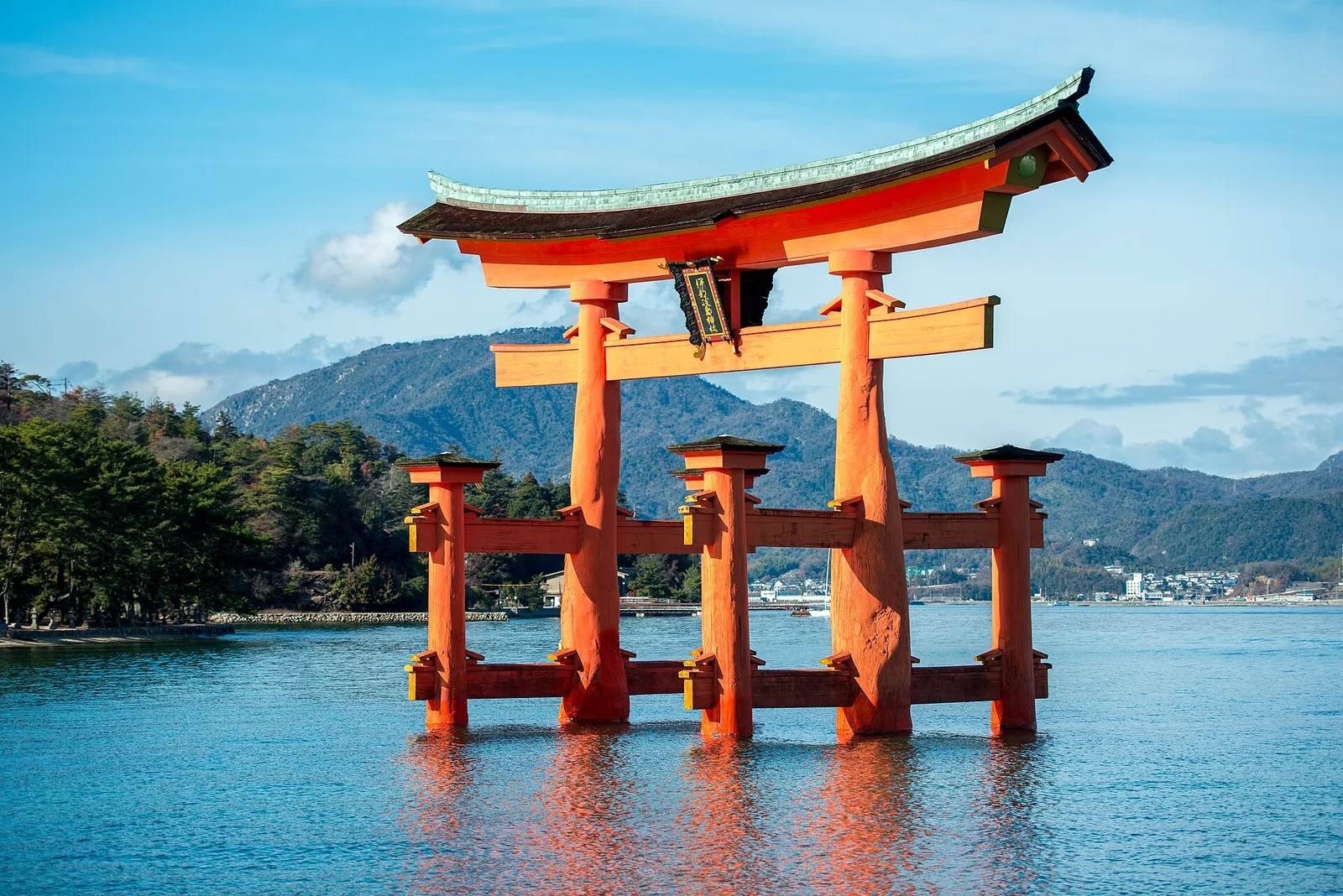 The great red torii gate of Itsukushima Shrine standing in the water with forested hills behind