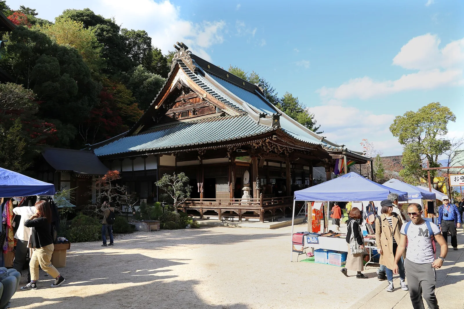 A wooden hall with a tiled roof at Daisho-in Temple, with visitors and small stalls in front