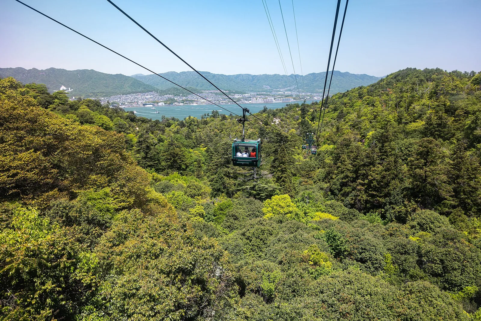 A ropeway cabin crossing above forested slopes on Miyajima, with the sea in the distance