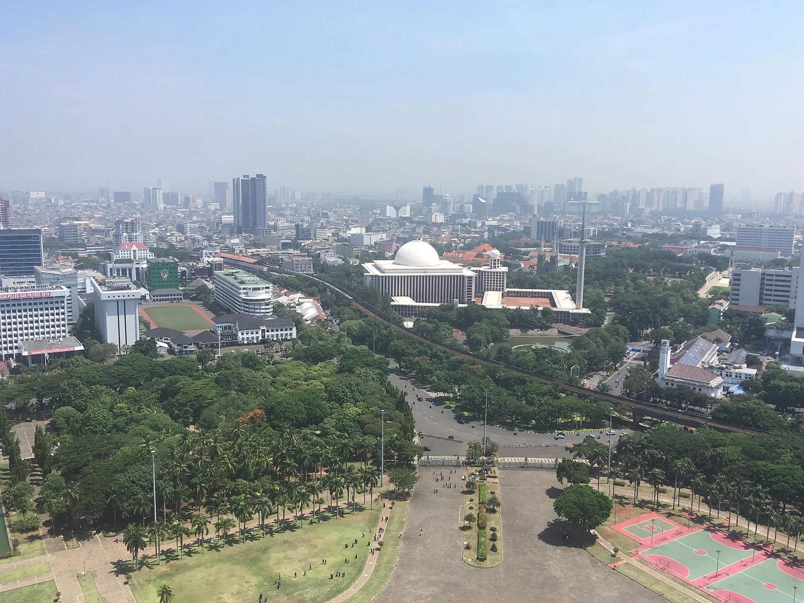 An aerial view over the Monas park toward the white dome and minaret of Istiqlal Mosque