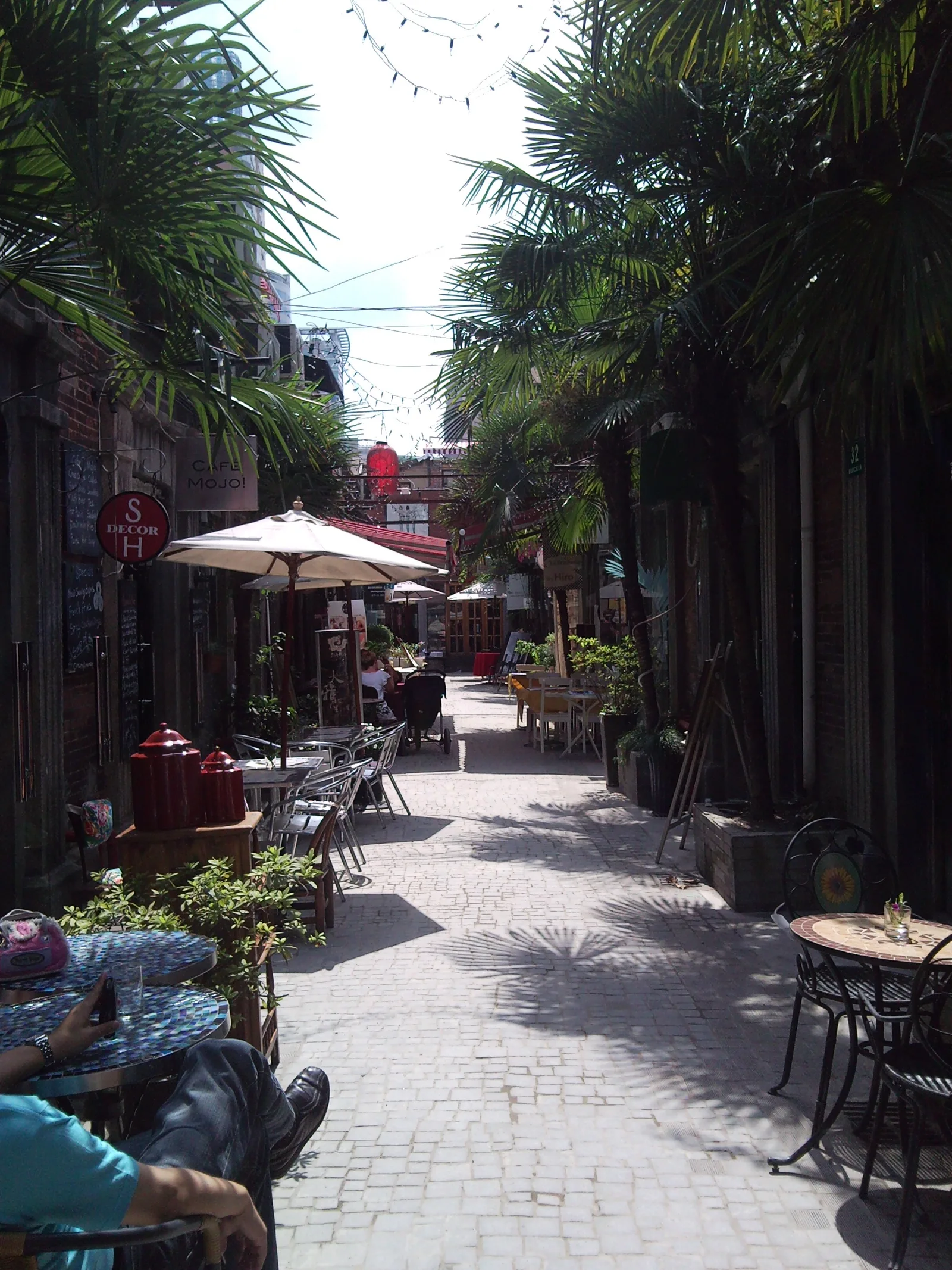 A cobbled Tianzifang lane with cafe tables under palm trees