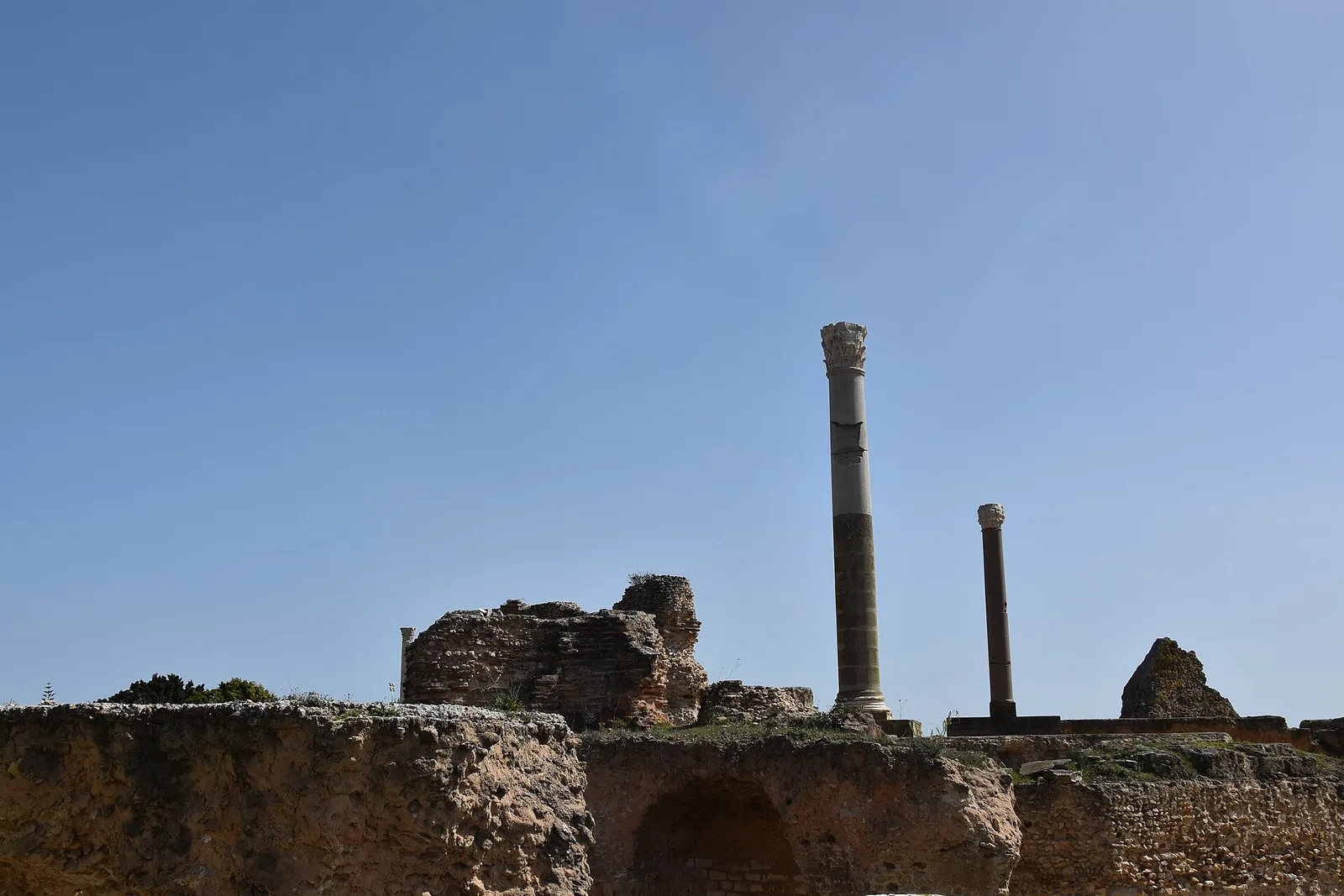Two tall Roman columns and brick ruins of the Antonine Baths under a blue sky