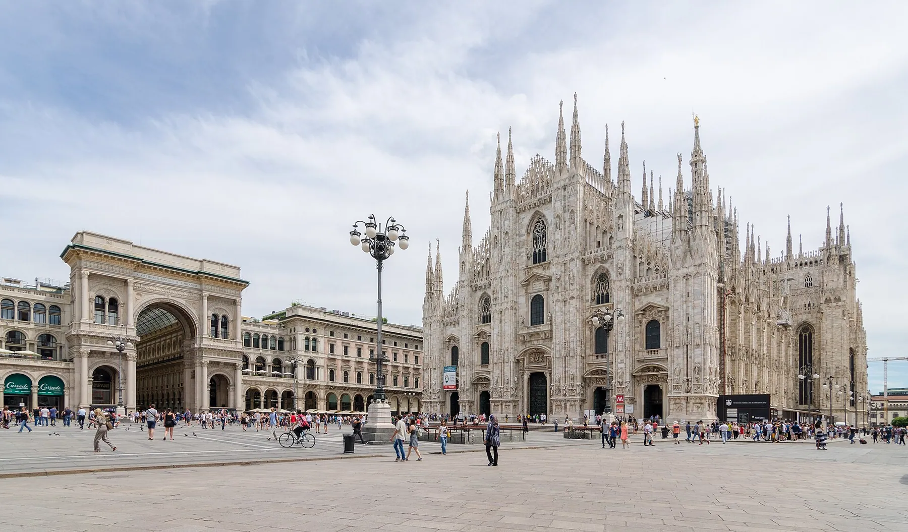 Milan Cathedral’s white marble facade across Piazza del Duomo, beside the arch of the Galleria Vittorio Emanuele II