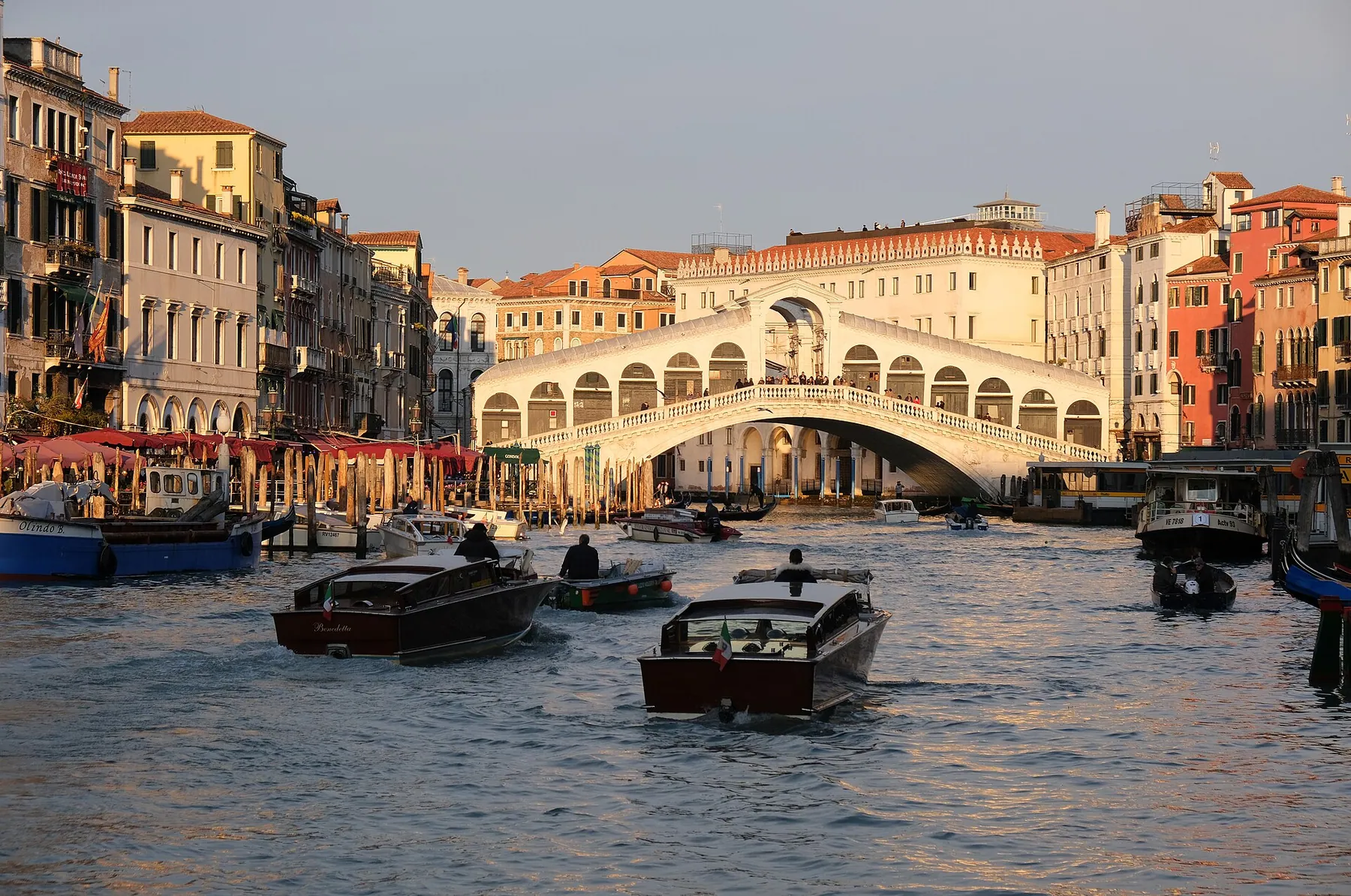 The Rialto Bridge arching over the Grand Canal in Venice, with boats and waterfront palaces in warm light