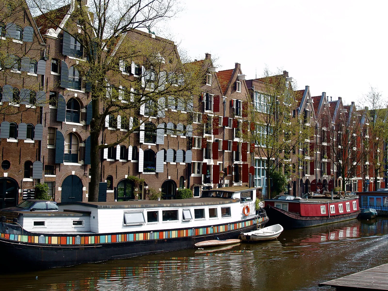 Rows of tall brick canal houses along an Amsterdam canal, with a houseboat moored in front