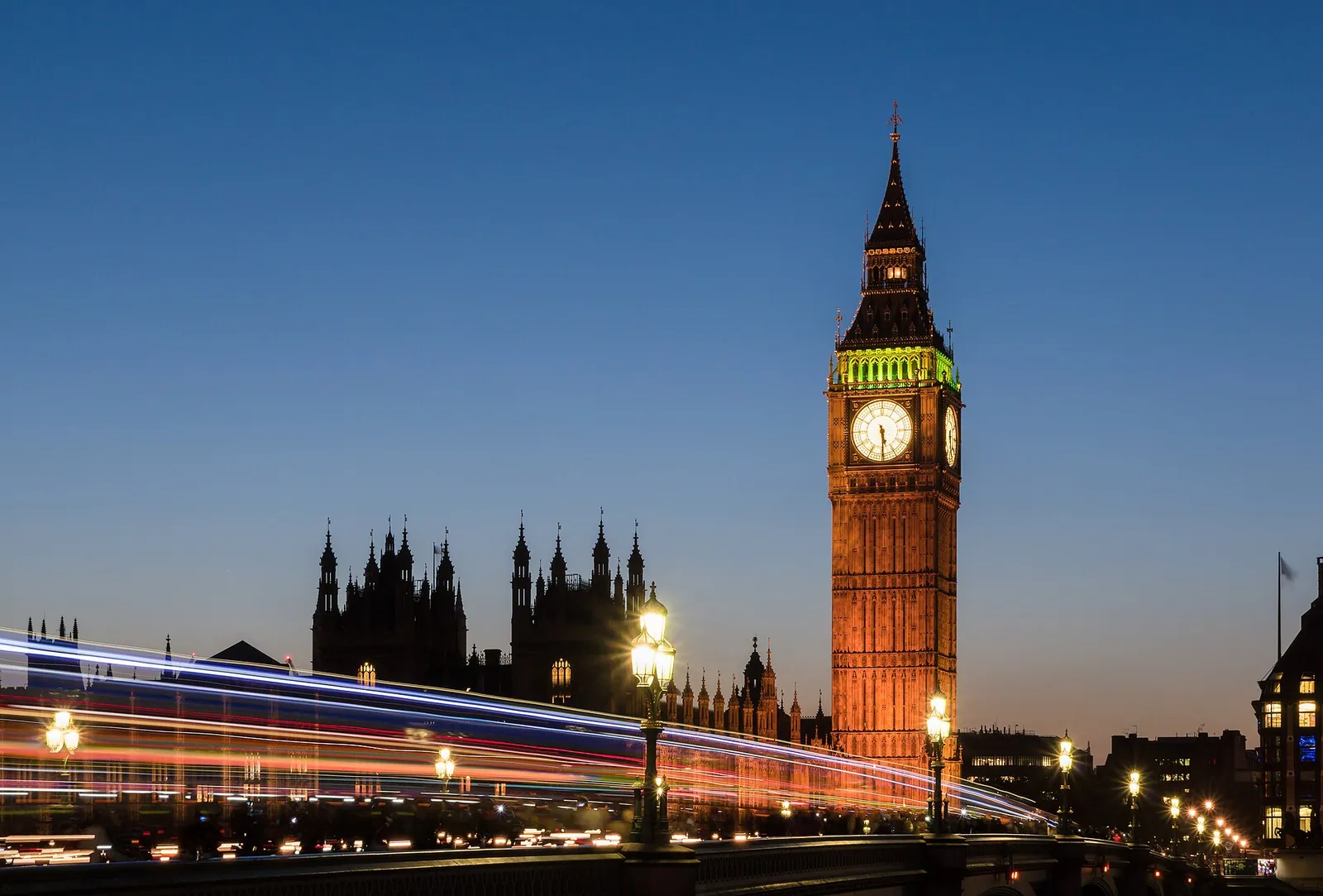 Big Ben’s clock tower lit against a deep blue dusk sky in London, with the Houses of Parliament in silhouette and streaks of traffic light below