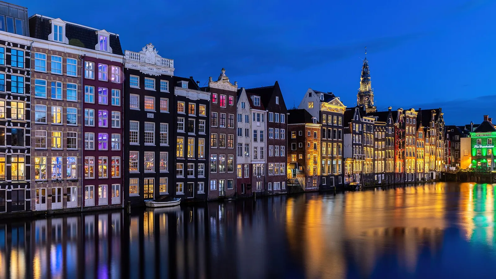 Narrow canal houses with lit windows reflected in the water at blue hour along the Damrak in Amsterdam