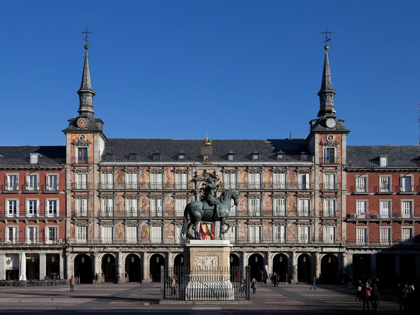 The arcaded ochre-and-red facade of Madrid’s Plaza Mayor, with its two slender towers and a statue at the center of the square